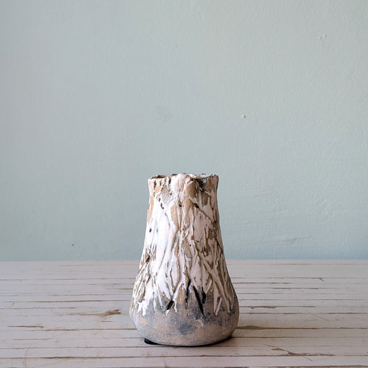 Front view of a beige stoneware vase with thick black and white glaze and vertical scoring, resembling the surface of tree bark.