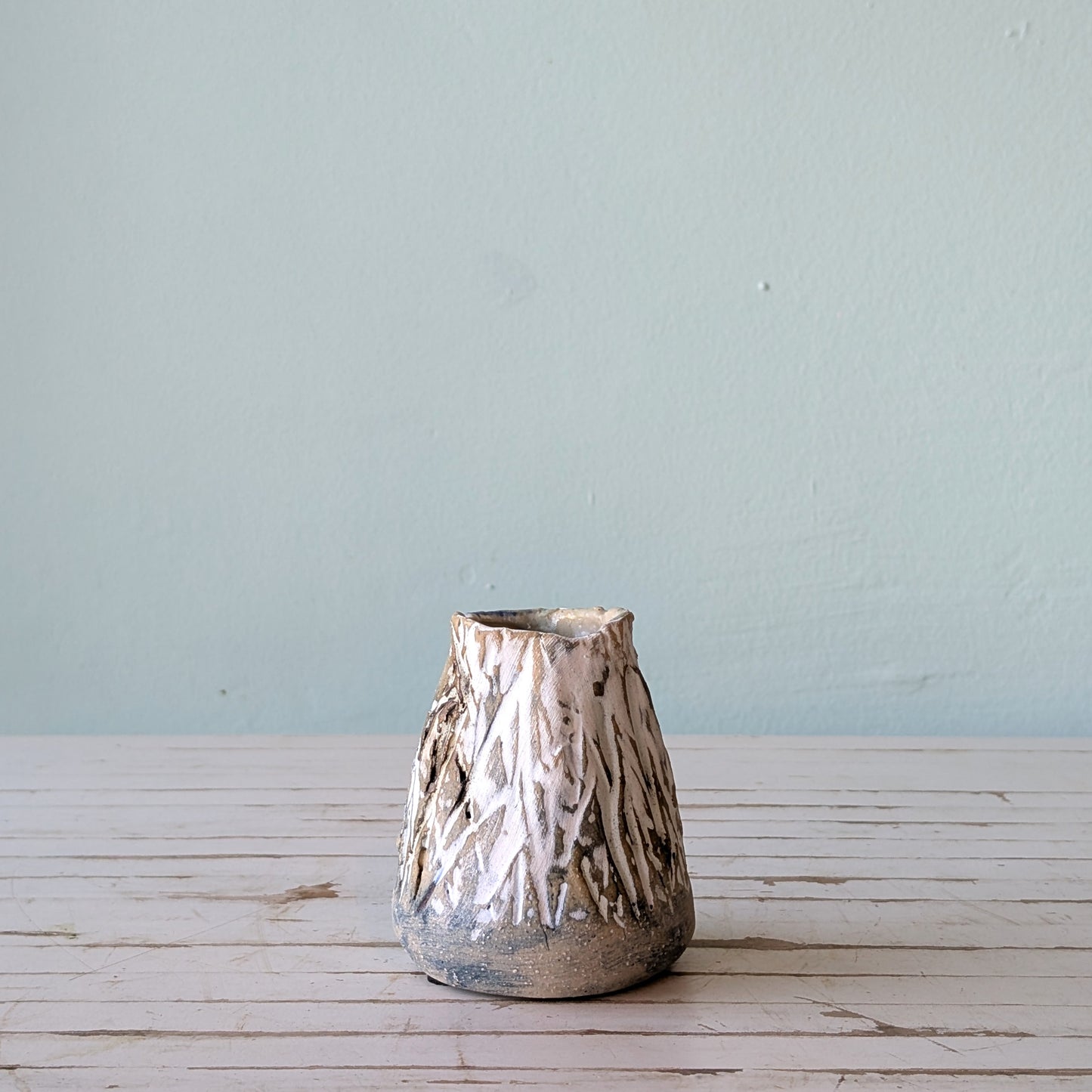Front view of a beige stoneware vase with thick black and white glaze and vertical scoring, resembling the surface of tree bark.