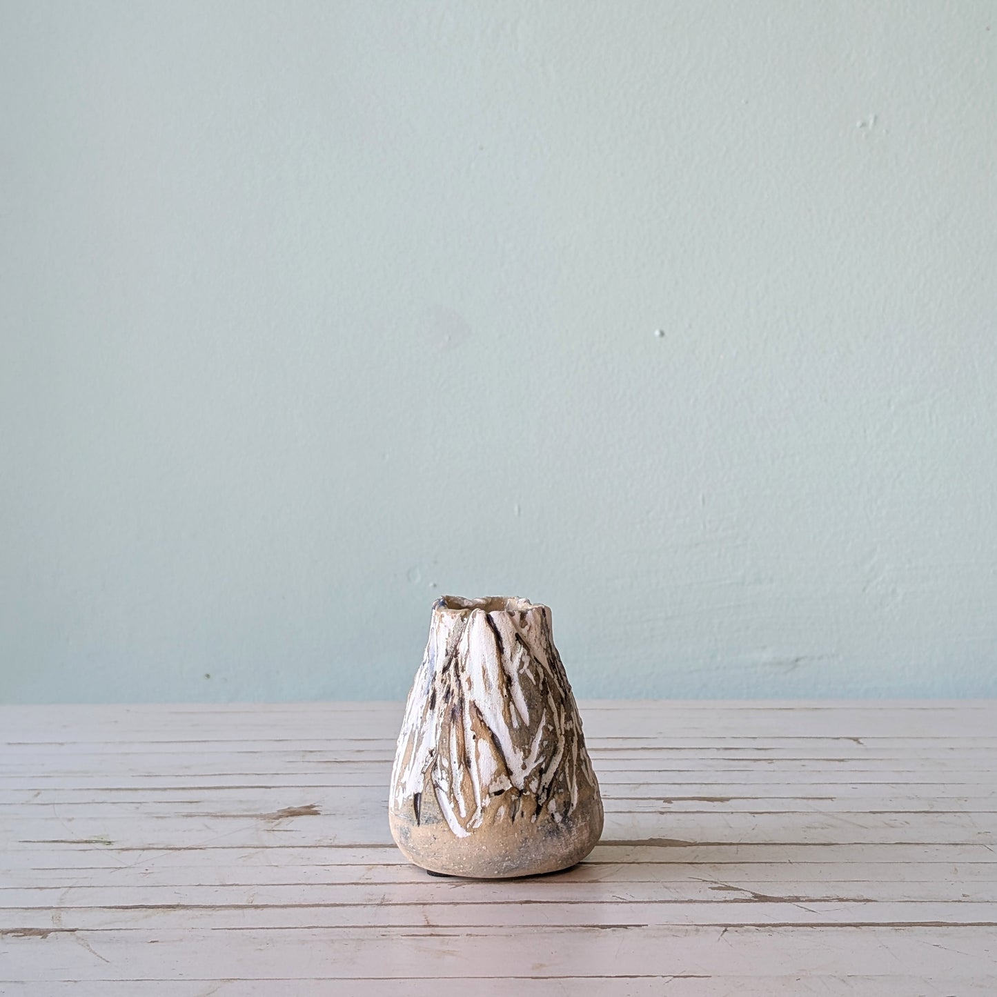 Front view of a beige stoneware vase with thick black and white glaze and vertical scoring, resembling the surface of tree bark.