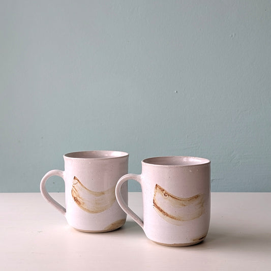 Two white mugs with brown brushstrokes pattern on a white table against a blue background.