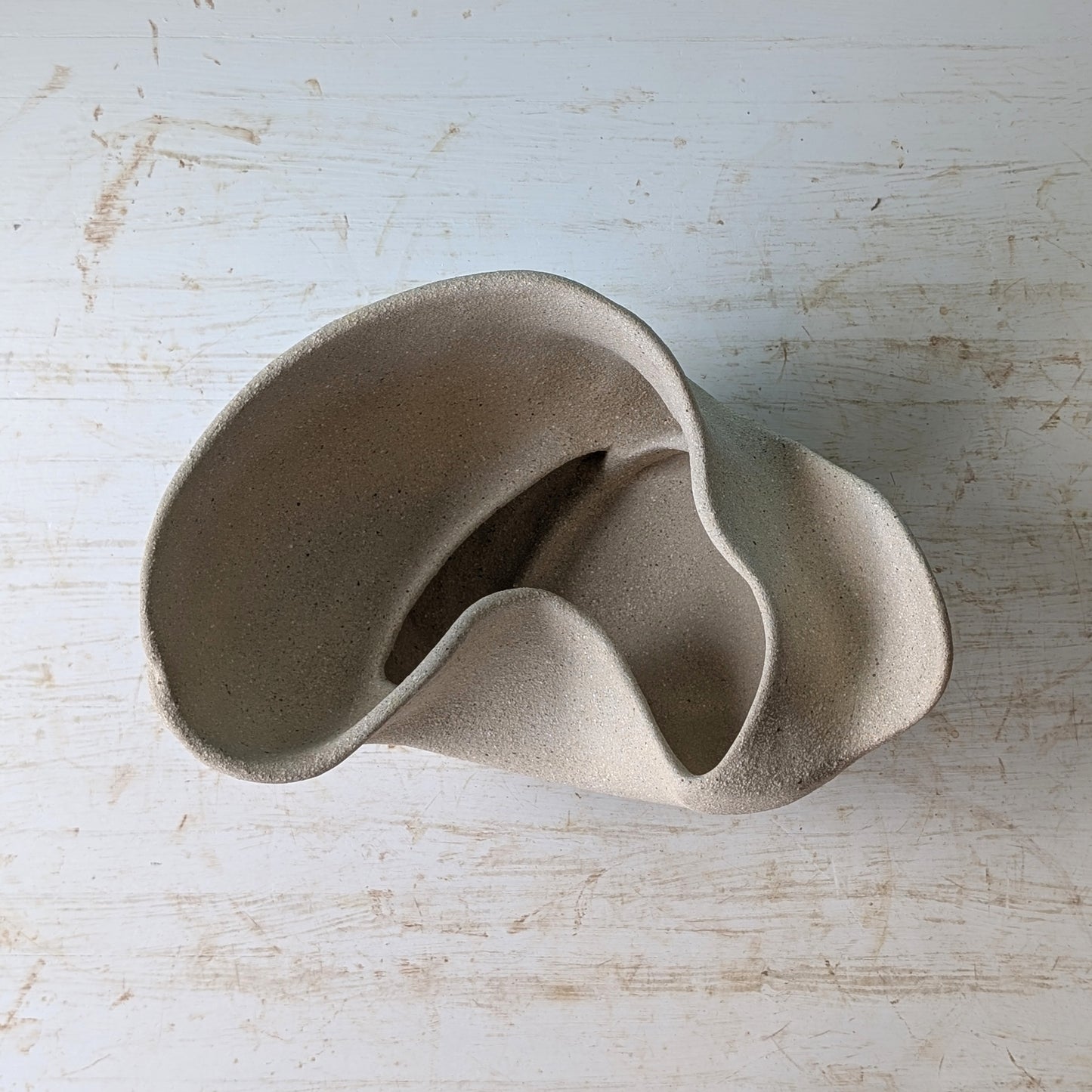 Sculptural bowl made of beige matte ceramic on a white table against a blue wall.