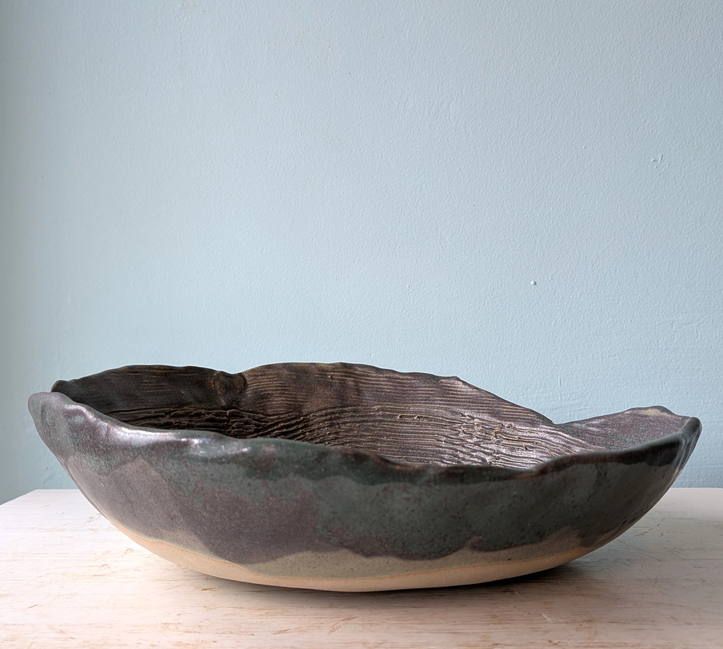 Large green and beige ceramic bowl on a white table against a blue wall.