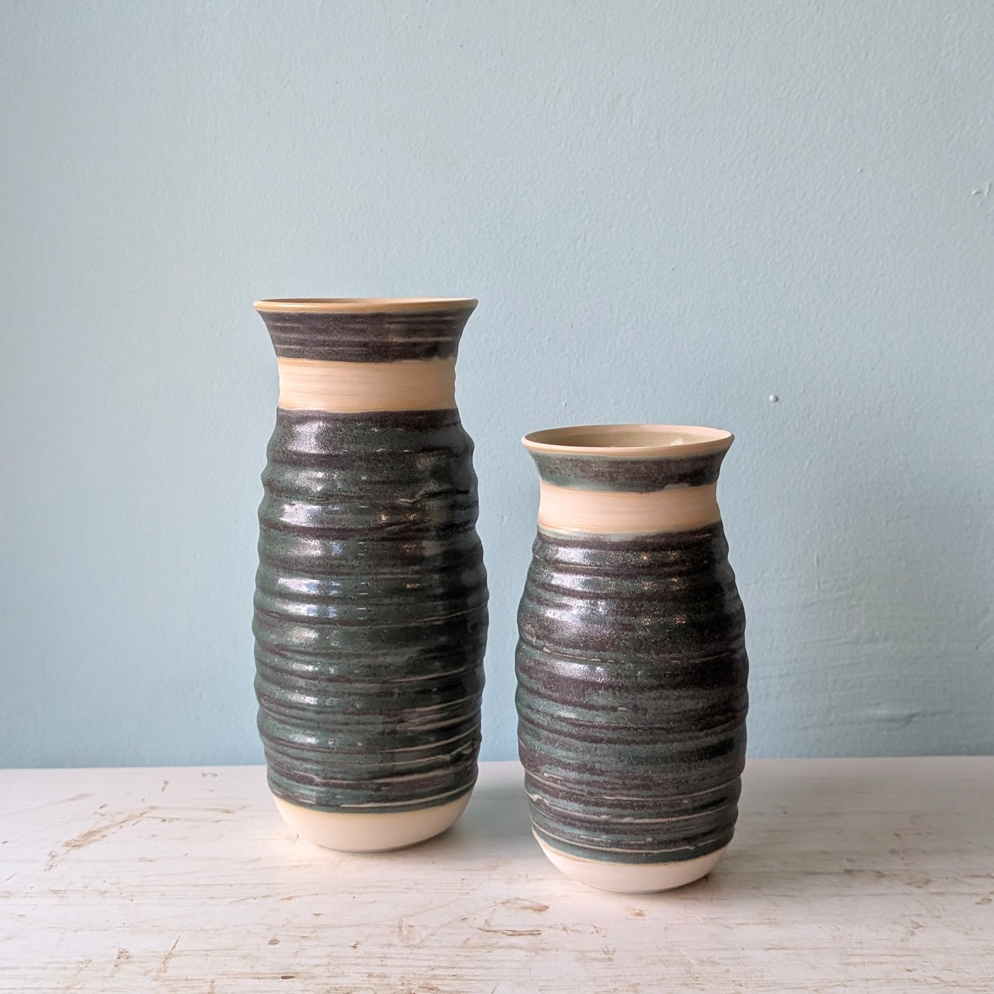 Two bottle green vases on a white table against a blue wall.