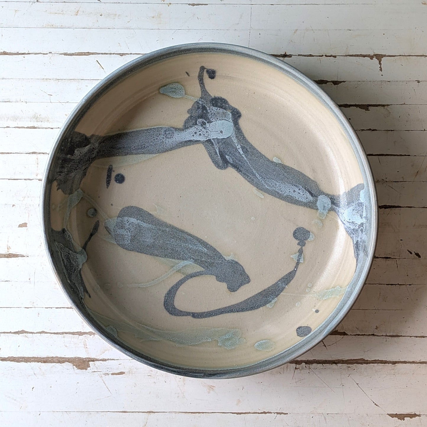Top view of a blue and green ceramic serving bowl on a white wooden table.