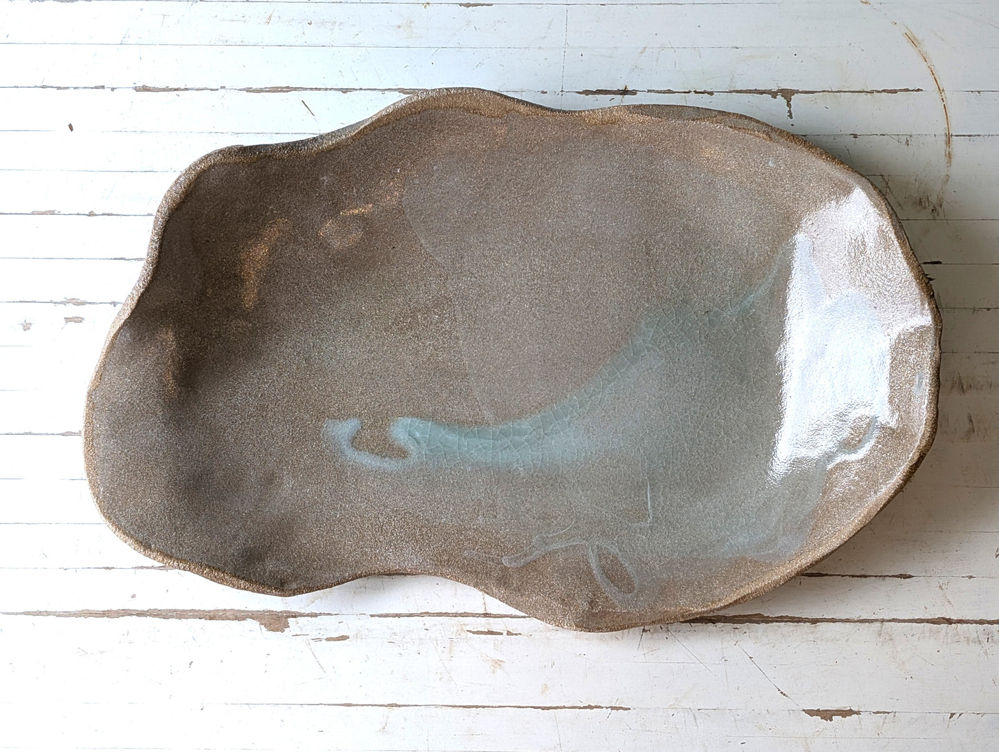 Top view of a freeform ceramic serving platter on a white wooden table.