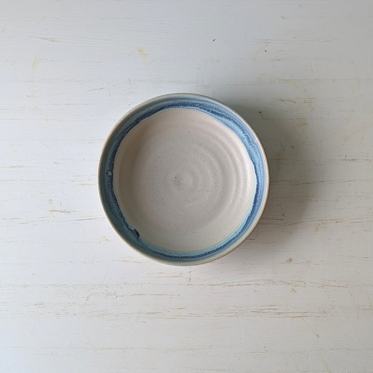 Top view of a beige serving bowl with blue/green edge on a white wooden table