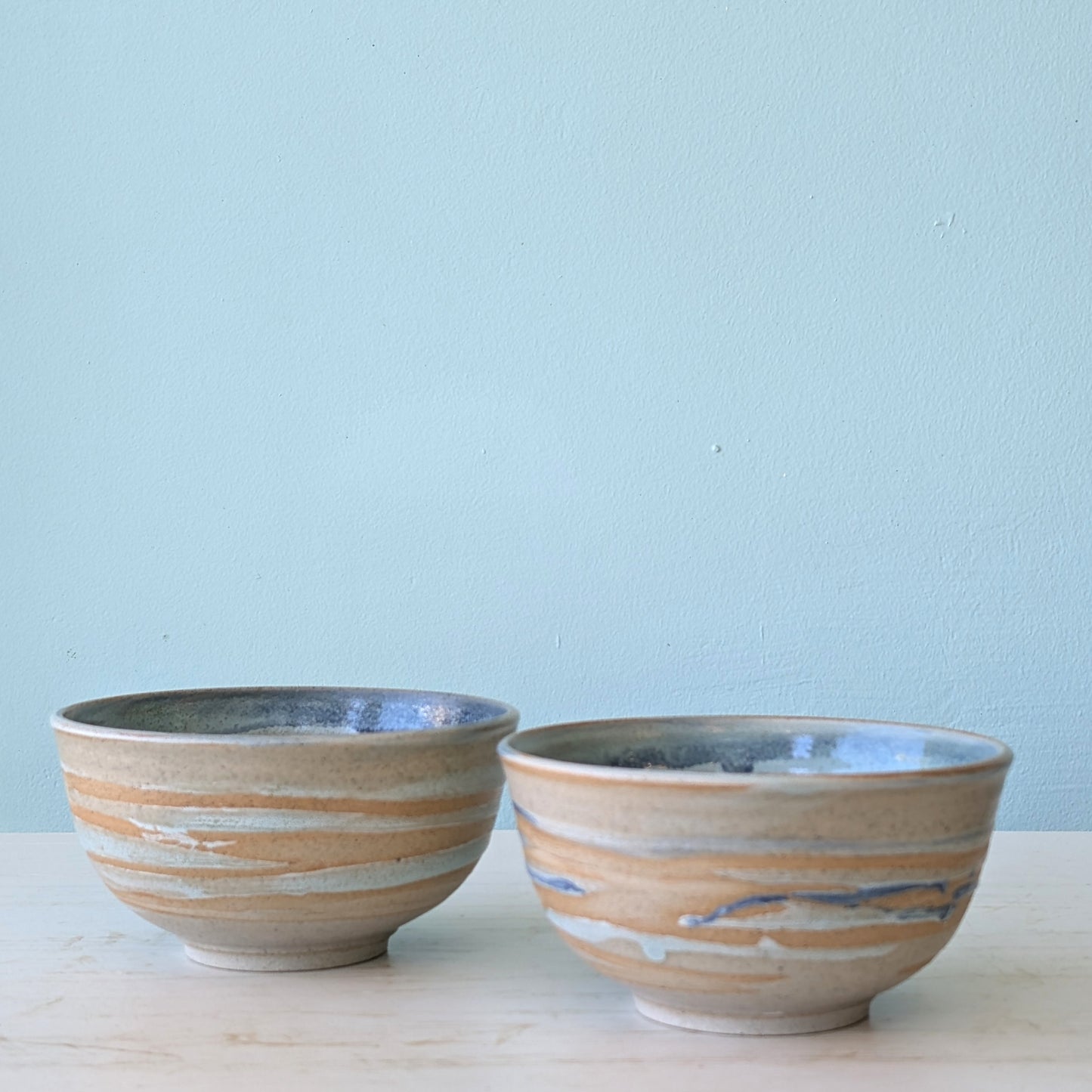 Two beige and blue ceramic bowls on a white table against a blue wall