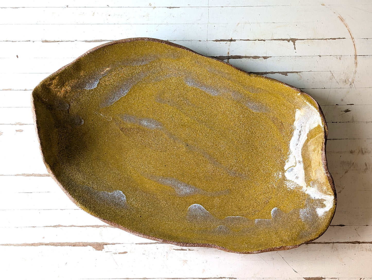 Top view of a freeform yellow ceramic platter on a white wooden table.