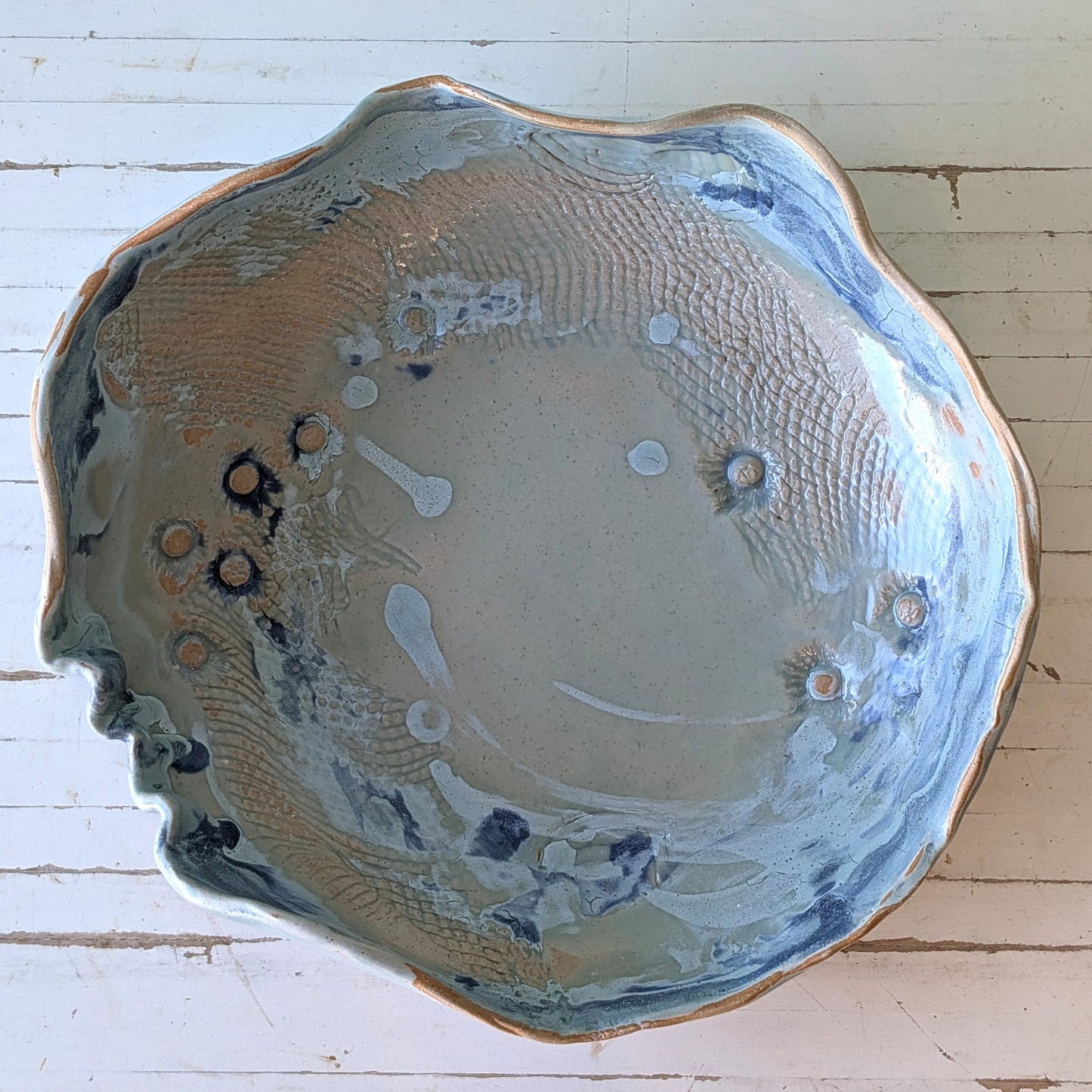 Hand built ceramic platter with shell indentations and blue glaze rim, viewed from above