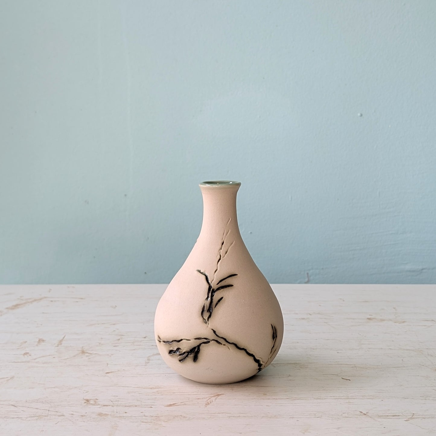 Ceramic vase with green seagrass pattern on a light wooden surface and blue background
