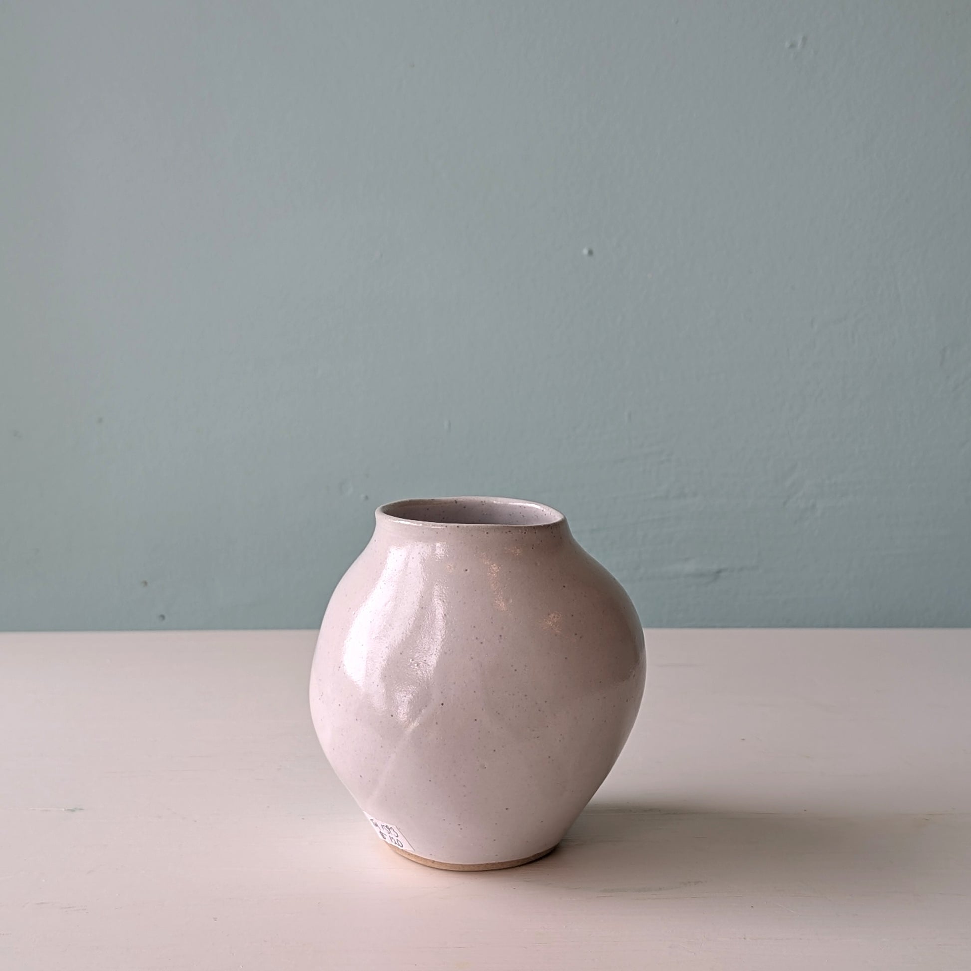 Beige ceramic vase on a white surface with a light blue wall background