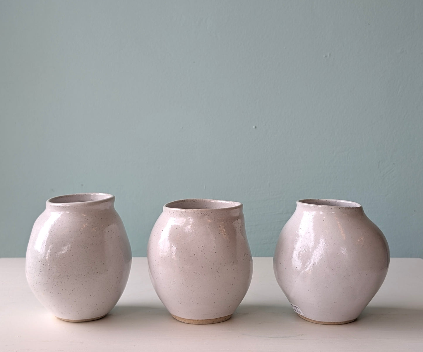 Three ceramic vases of similar design on a light surface with a light blue wall background