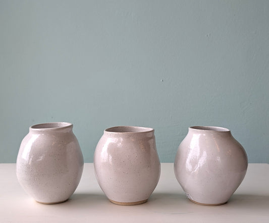 Three ceramic vases of similar design on a light surface with a light blue wall background