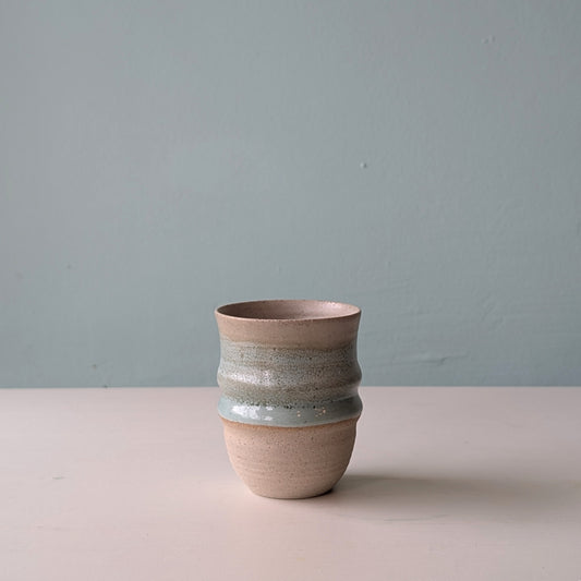 Beige ceramic cup with green glaze on a white table against a blue background.