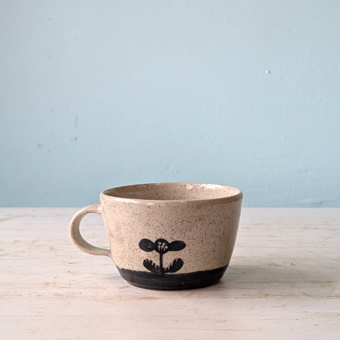 Ceramic mug with a black floral design on a light wooden surface and light blue background