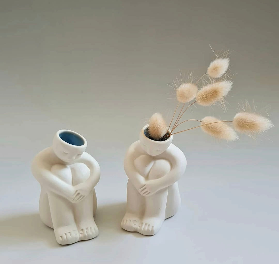 Two ceramic bud vases in the shape of seated figures against a white background.