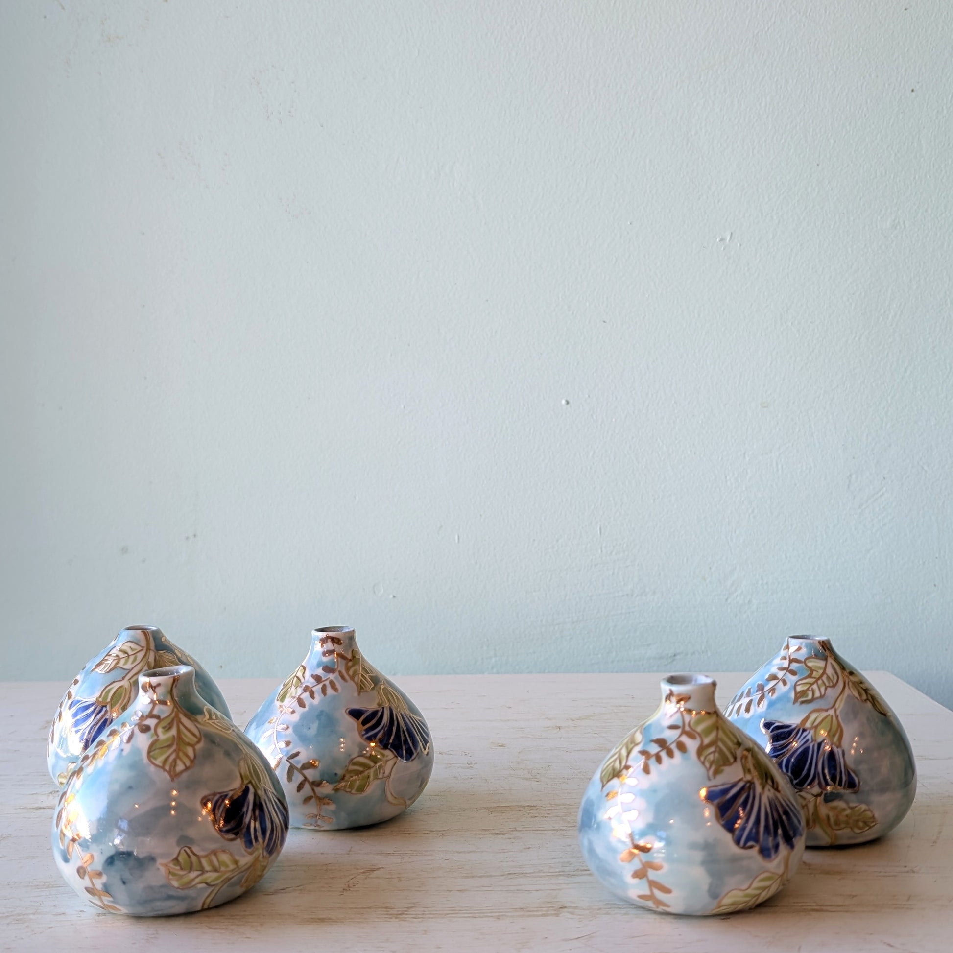 5 porcelain vases with blue batik deisgn and gold highlights on a white table against a blue background