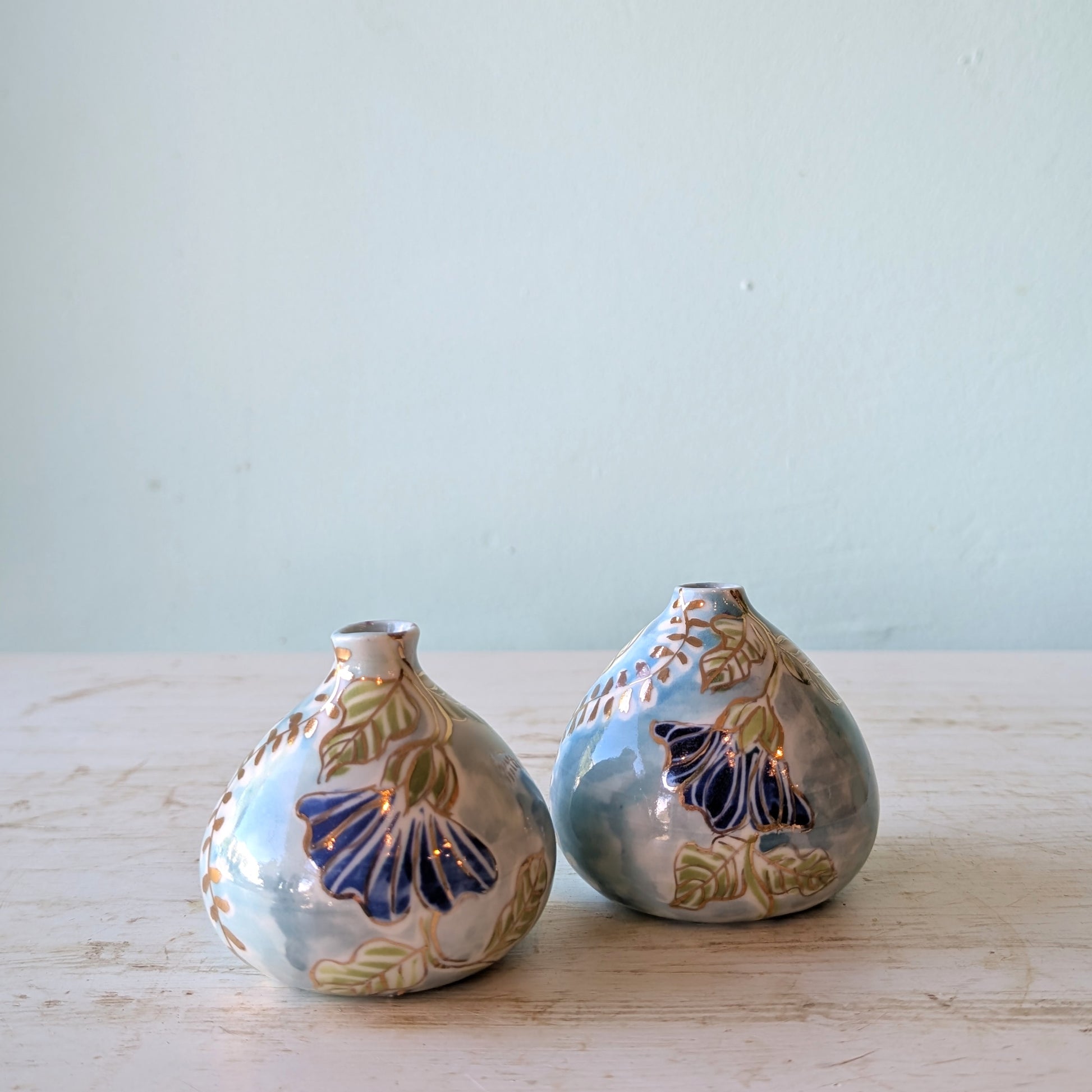 Two ceramic vases with batik floral designs on a light wooden surface and light blue background