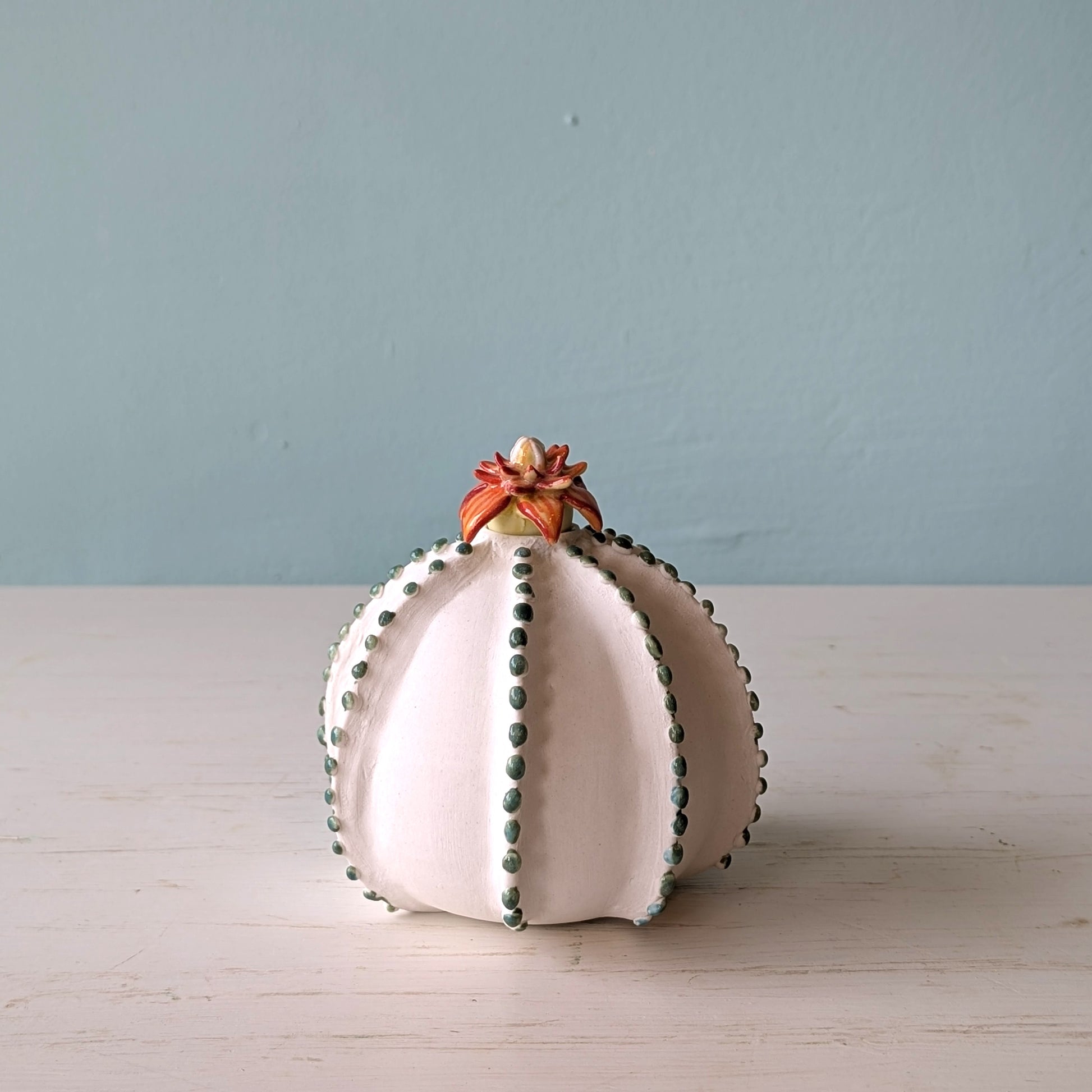 Decorative white vase with green dots on a light wooden surface and blue wall background