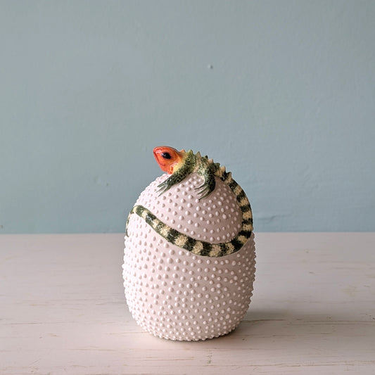 White porcelain vase with lizard design on white table against blue wall