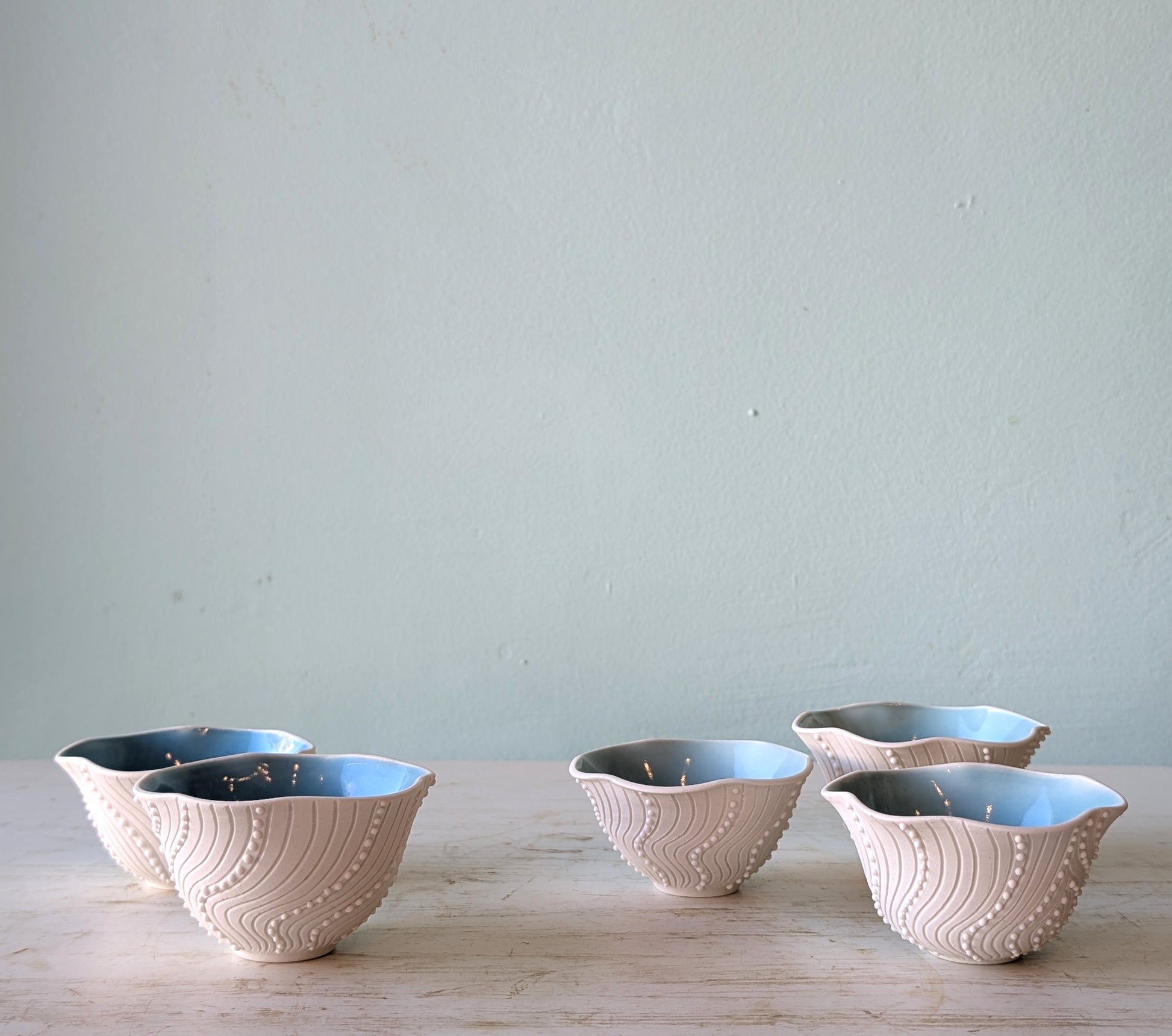 5 frilled porcelain dishes with blue interior on a white table against a blue wall