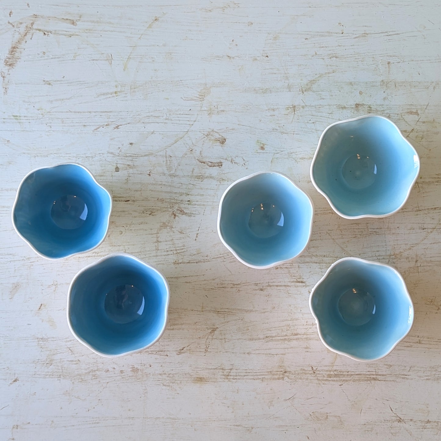 Five small blue ceramic dishes on a light wooden surface