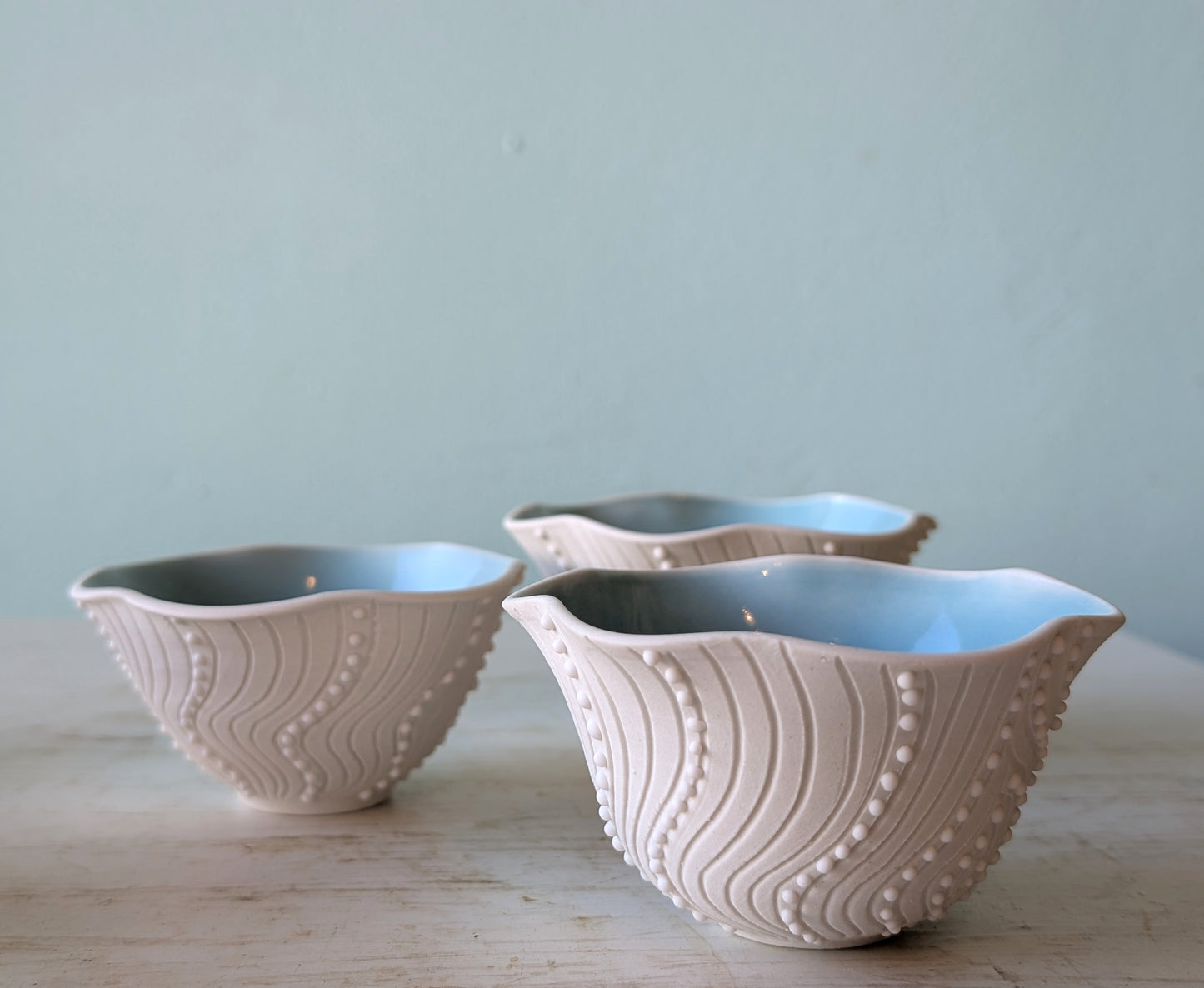Three ceramic bowls with textured designs on a wooden surface and light blue background