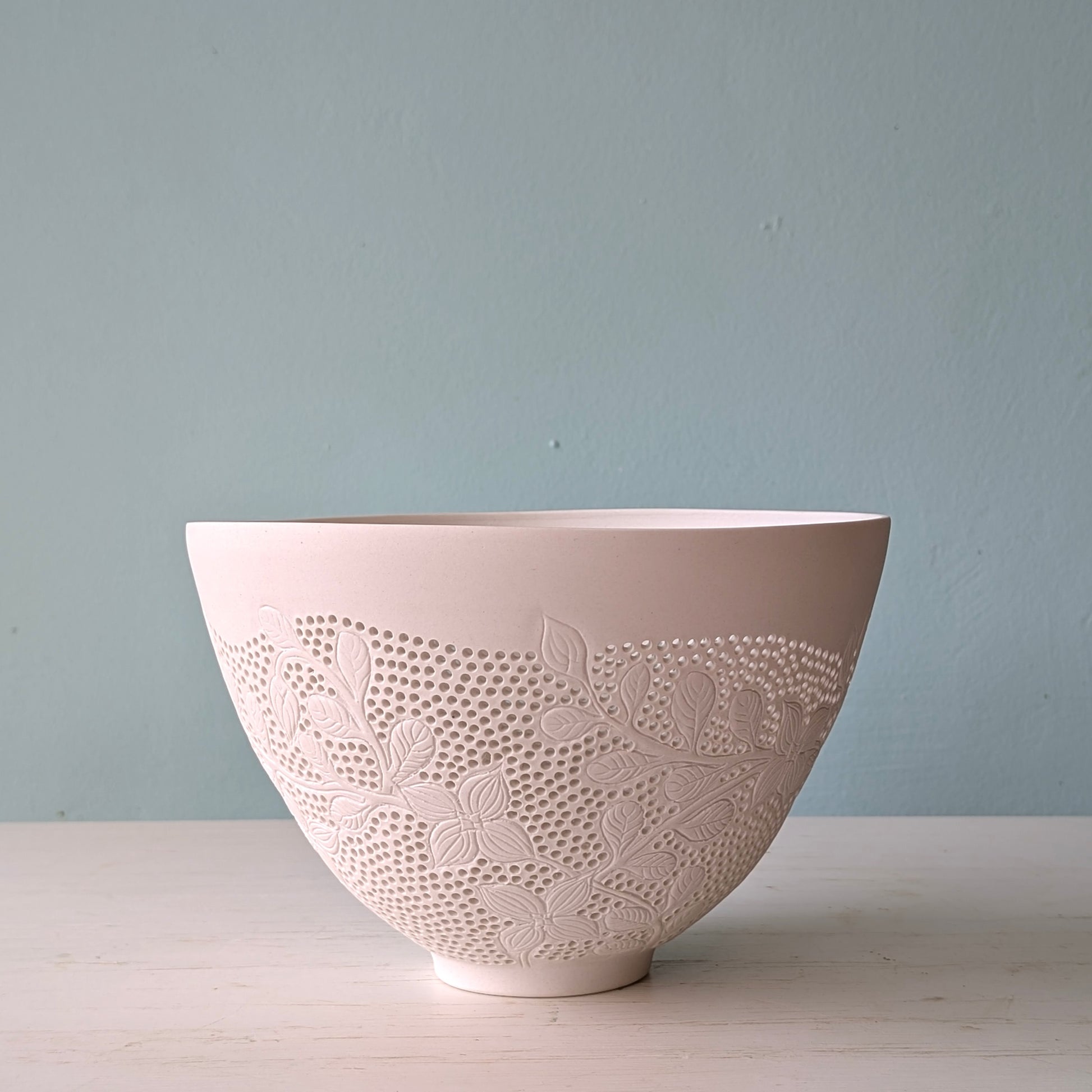 Decorative ceramic bowl with carved floral patterns on a light blue background
