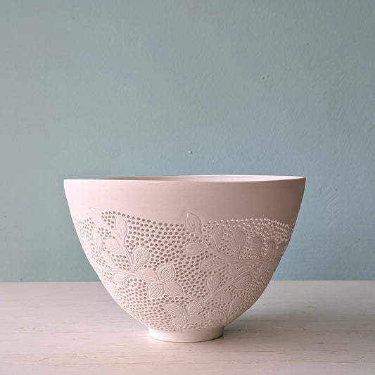 Decorative ceramic bowl with carved floral patterns on a light blue background