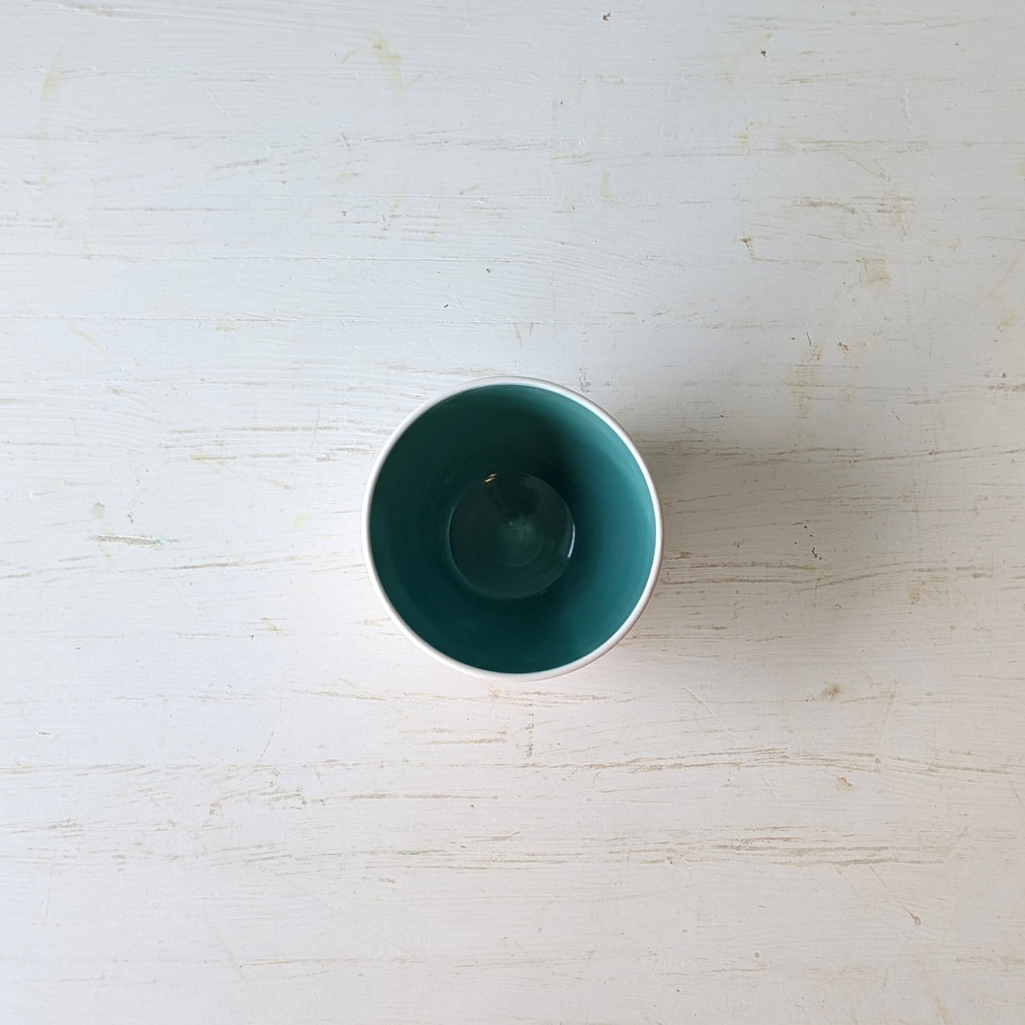 White porcelain bowl with teal interior on a light wooden surface
