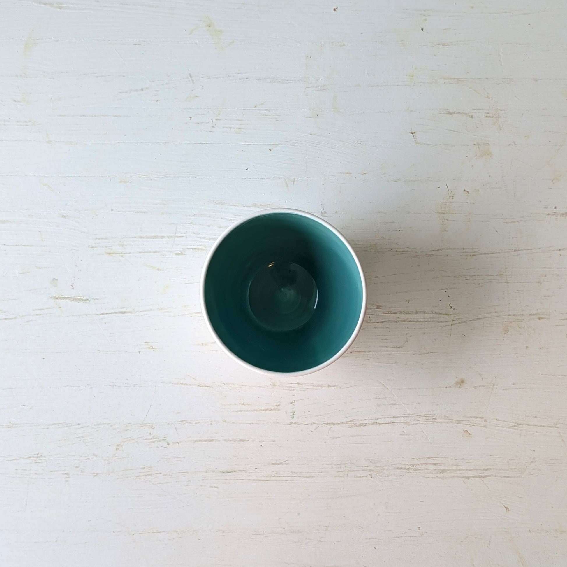 White porcelain bowl with teal interior on a light wooden surface