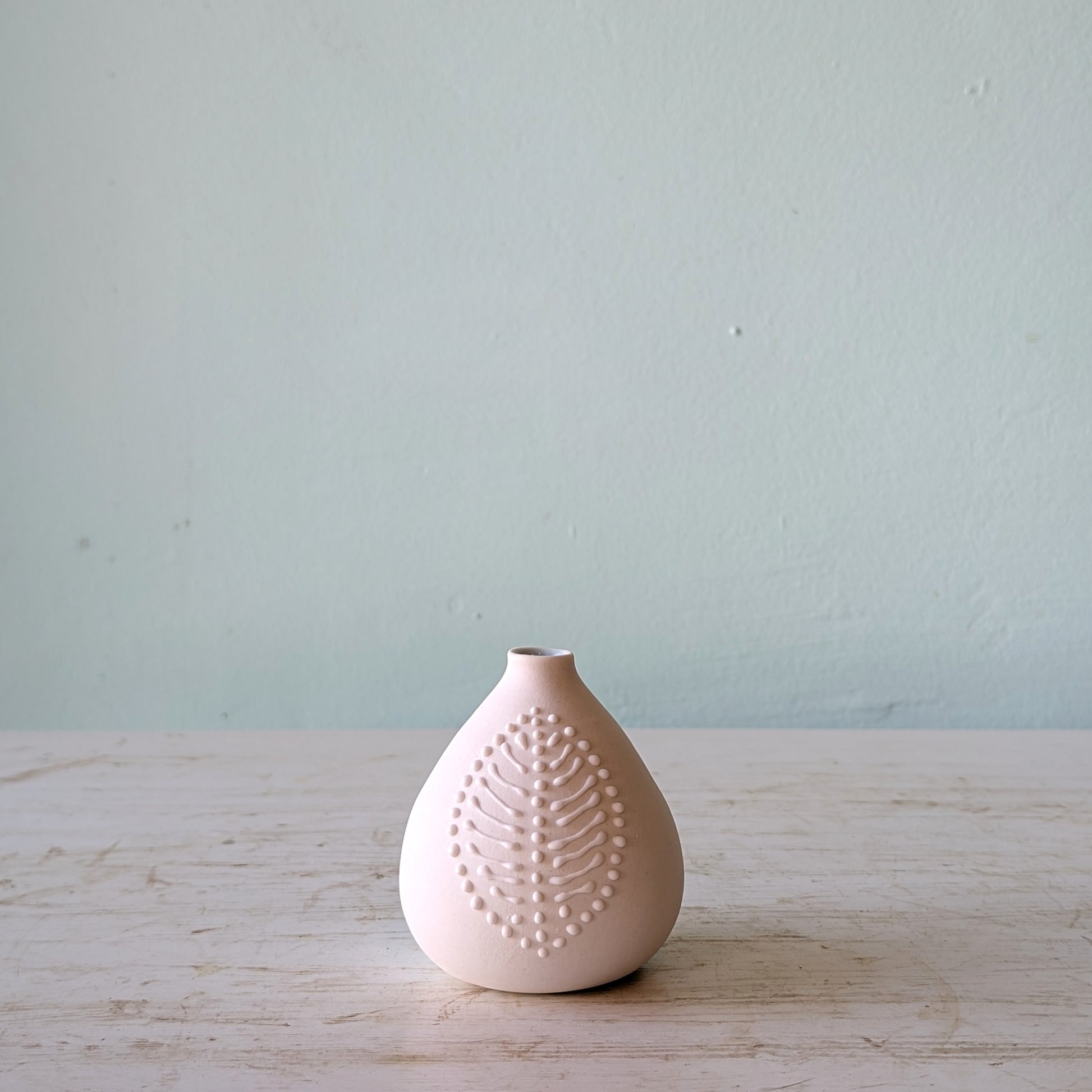 White ceramic vase with textured design on a light wooden surface and blue background