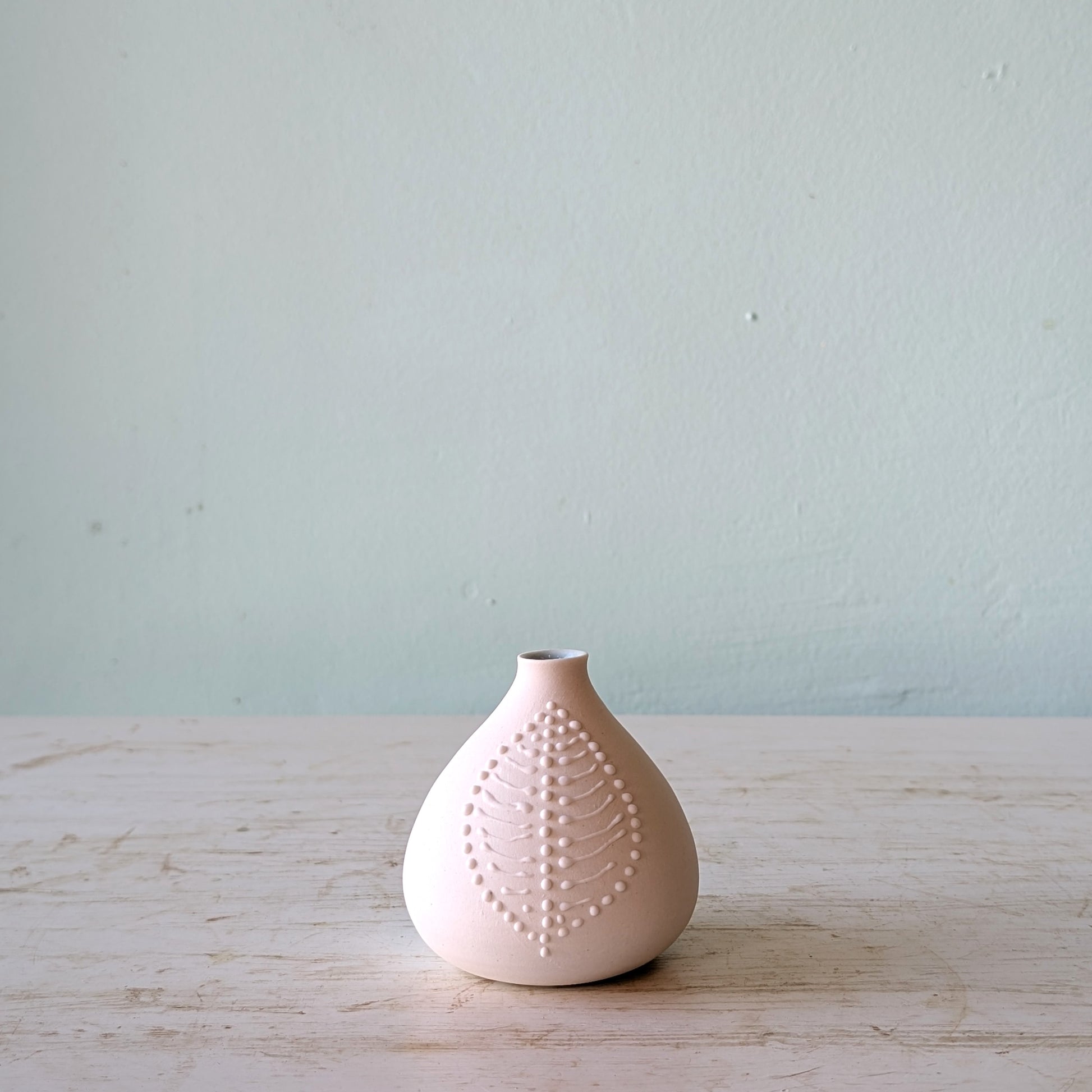 White ceramic vase with textured surface on a light wooden table against a light blue wall.