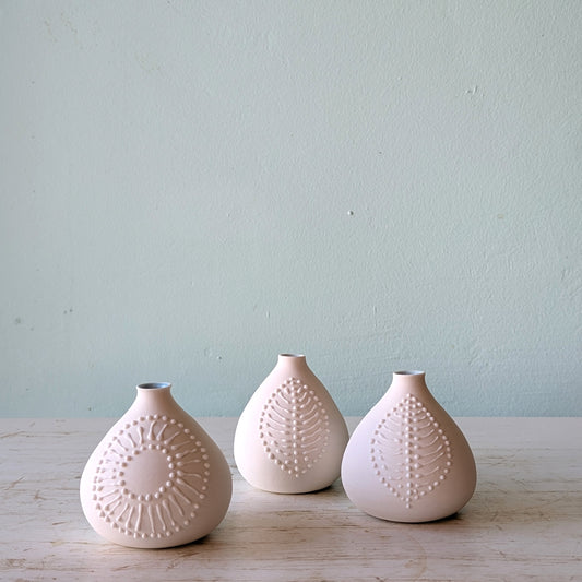 Three white textured vases on a wooden surface with a light blue background