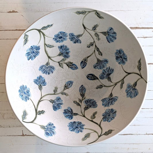 Top view of a large white porcelain bowl with blue flower pattern and carving