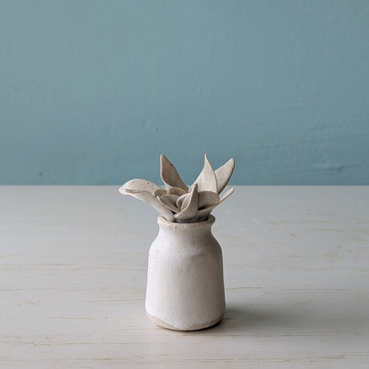 Small ceramic bottle with leaf shaped lid on a light wooden surface against a blue wall
