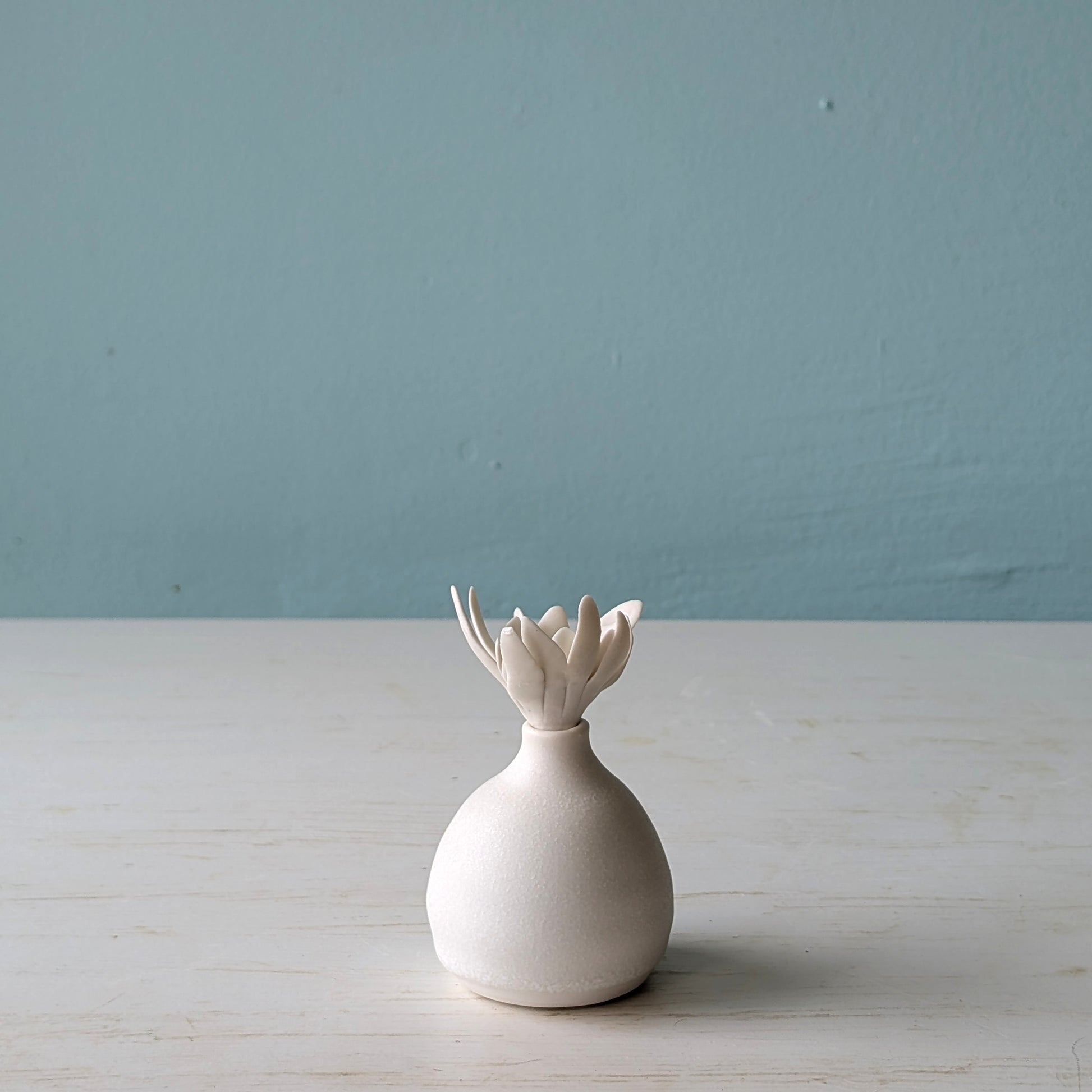 White ceramic bottle with a unique design on a light wooden surface against a blue wall.