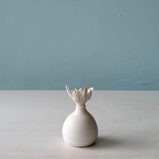 White ceramic bottle with a unique design on a light wooden surface against a blue wall.