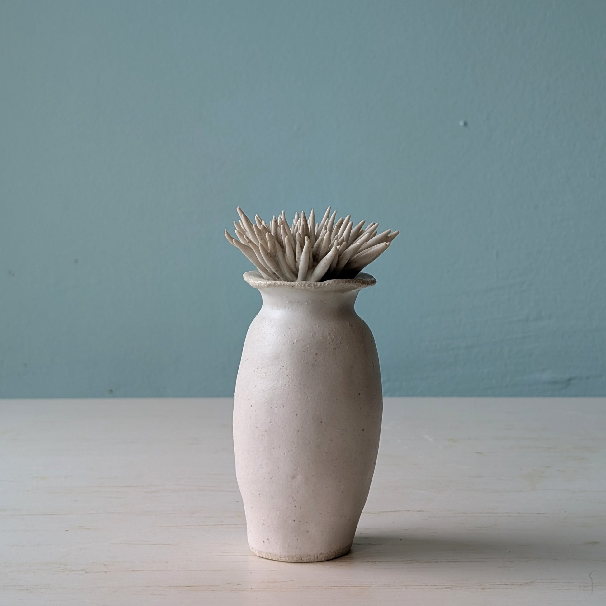 White ceramic bottle with plant shaped lid on a light wooden surface and blue wall background