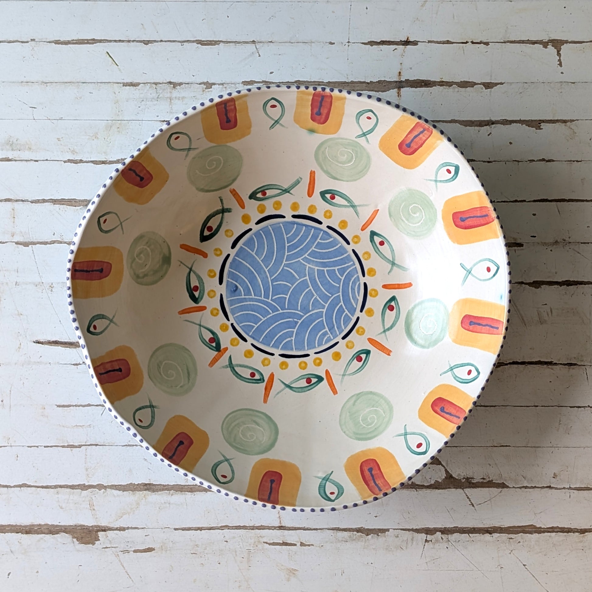 Top view of a colourful ceramic bow with fish design on a white wooden surface.