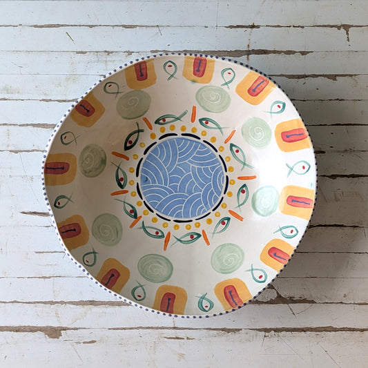 Top view of a colourful ceramic bow with fish design on a white wooden surface.