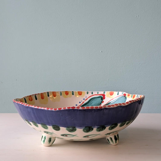 Multicoloured ceramic footed bowl on a white table against a blue wall