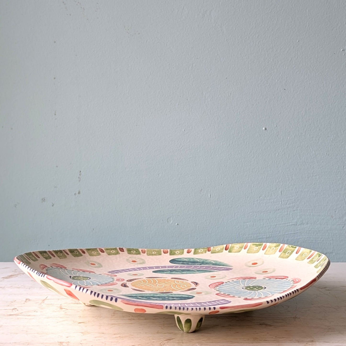 Decorative ceramic plate with colorful patterns on a wooden surface and light blue wall background