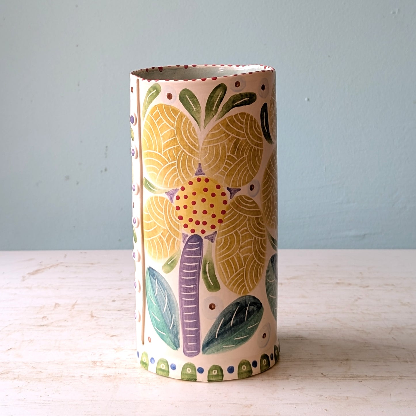 Cylindrical ceramic vase with colorful elephant design on a light wooden surface and light blue background