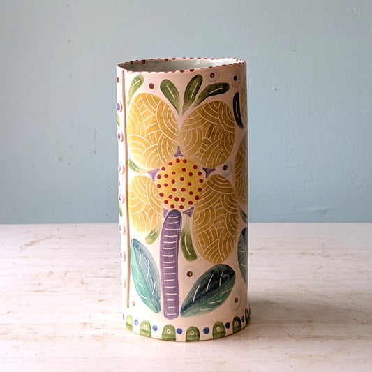 Cylindrical ceramic vase with colorful elephant design on a light wooden surface and light blue background