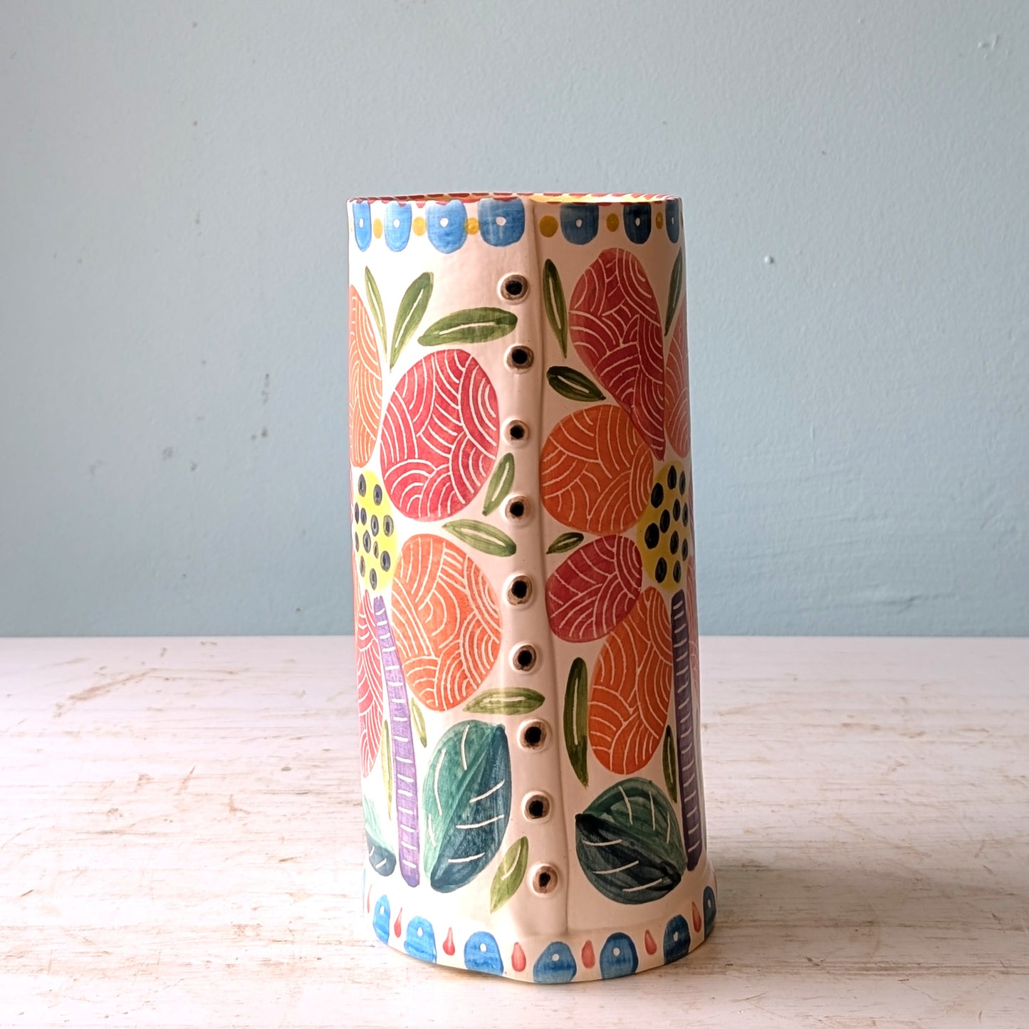 Colorful ceramic vase with floral patterns on a light wooden surface and light blue background