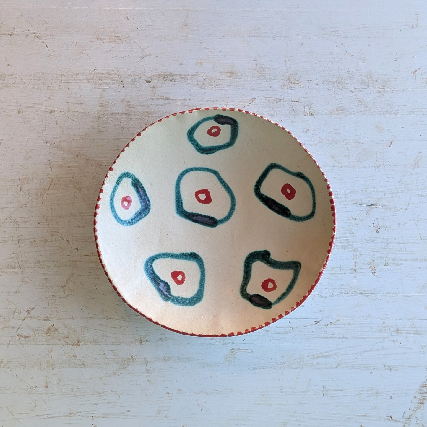 Top view of cream ceramic bowl white green and red circles, on a white wooden table.