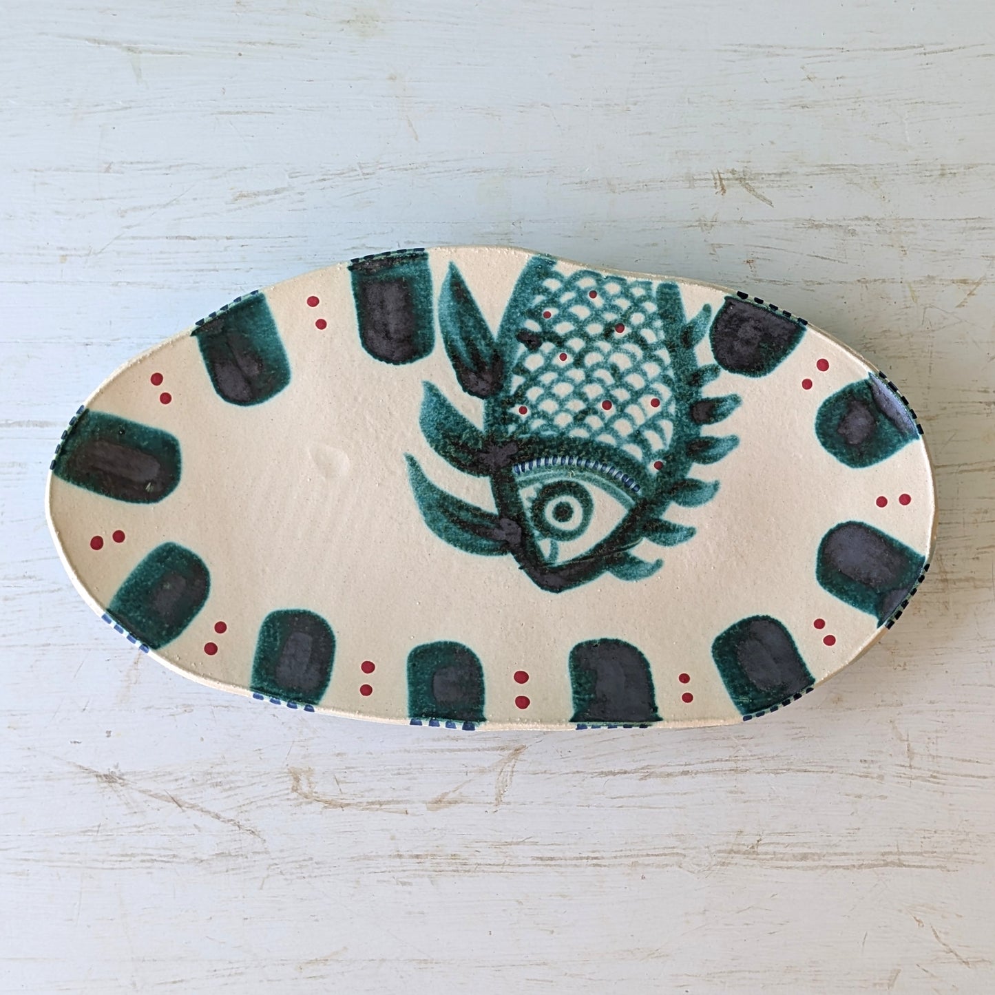 Decorative platter with a green fish design on a light wooden surface