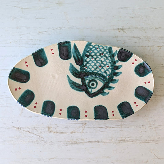 Decorative platter with a green fish design on a light wooden surface