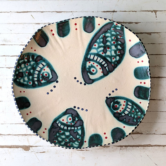 Top view of a white ceramic platter with green fish design on a white wooden background.